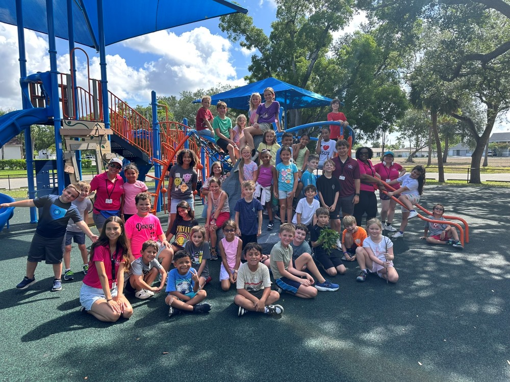 Group photo of children outside in the sun, posing on a playground set